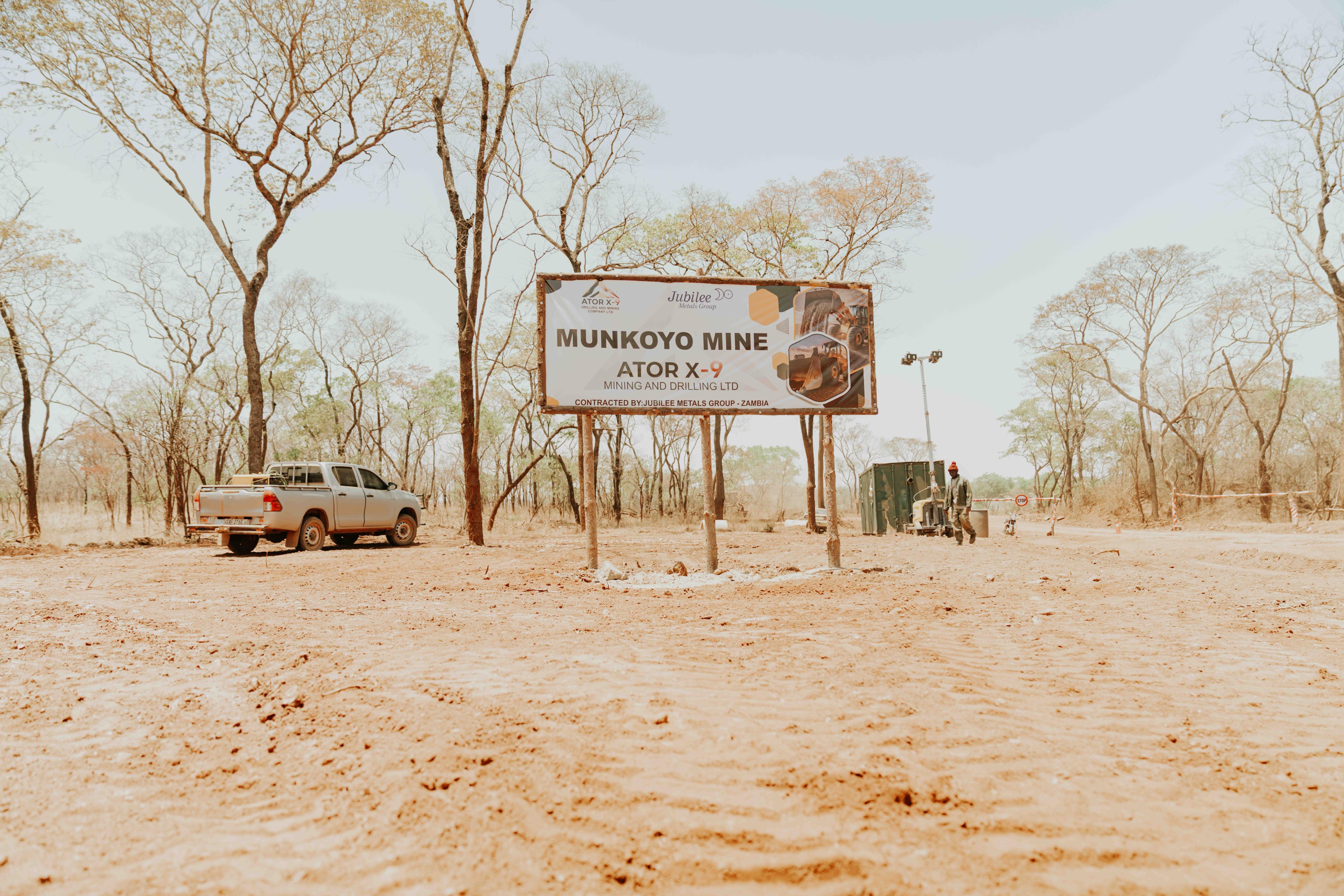 Two excavators actively working in a large open-pit mining site, surrounded by rugged earth and distant trees under a bright blue sky with scattered clouds. The scene conveys industrious activity and progress in the mining industry, highlighting the scale and machinery involved in resource extraction.